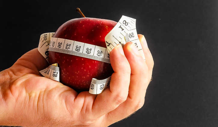 Person holding red apple with tape measure around it.